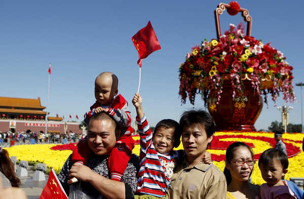 Visitors wave national flags in front of a bed of flowers at the Tian'anmen Square in Beijing on Sept 30. Zhu Xingxin / China Daily  Travel crush as Golden Week sets records