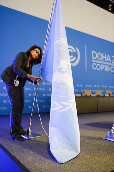 A woman installs a UN flag in the assembly room of the climate change conference at the Qatar National Convention Center in Doha on Nov 25, 2012,  Doha heats up for climate change conference